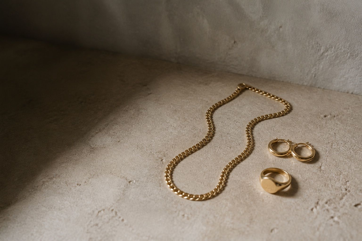 A gold curb chain, hoop earrings and a signet ring resting on limestone